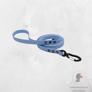 A light blue dog leash with a black carabiner clip and silver metal rivets, displayed on a textured light gray background with a 'Handmade in Lithuania' logo in the bottom right corner.