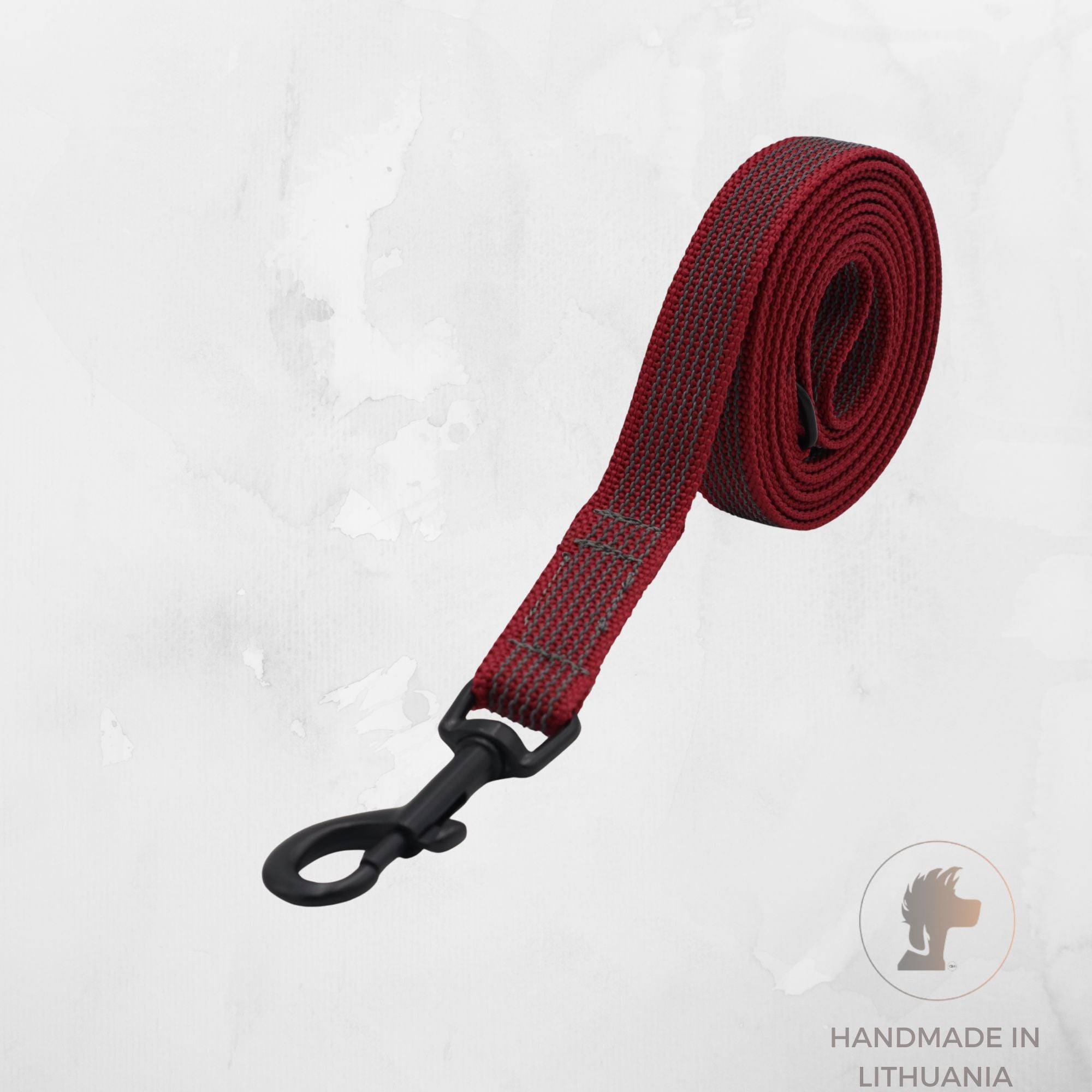 A dark red woven webbing dog leash with a black metal swivel snap hook, shown coiled on a light gray textured background with a 'Handmade in Lithuania' logo in the bottom right corner.