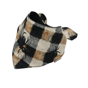 A triangular pet bandana featuring a black, brown, and cream plaid pattern with printed black spider designs, shown on a plain white background.