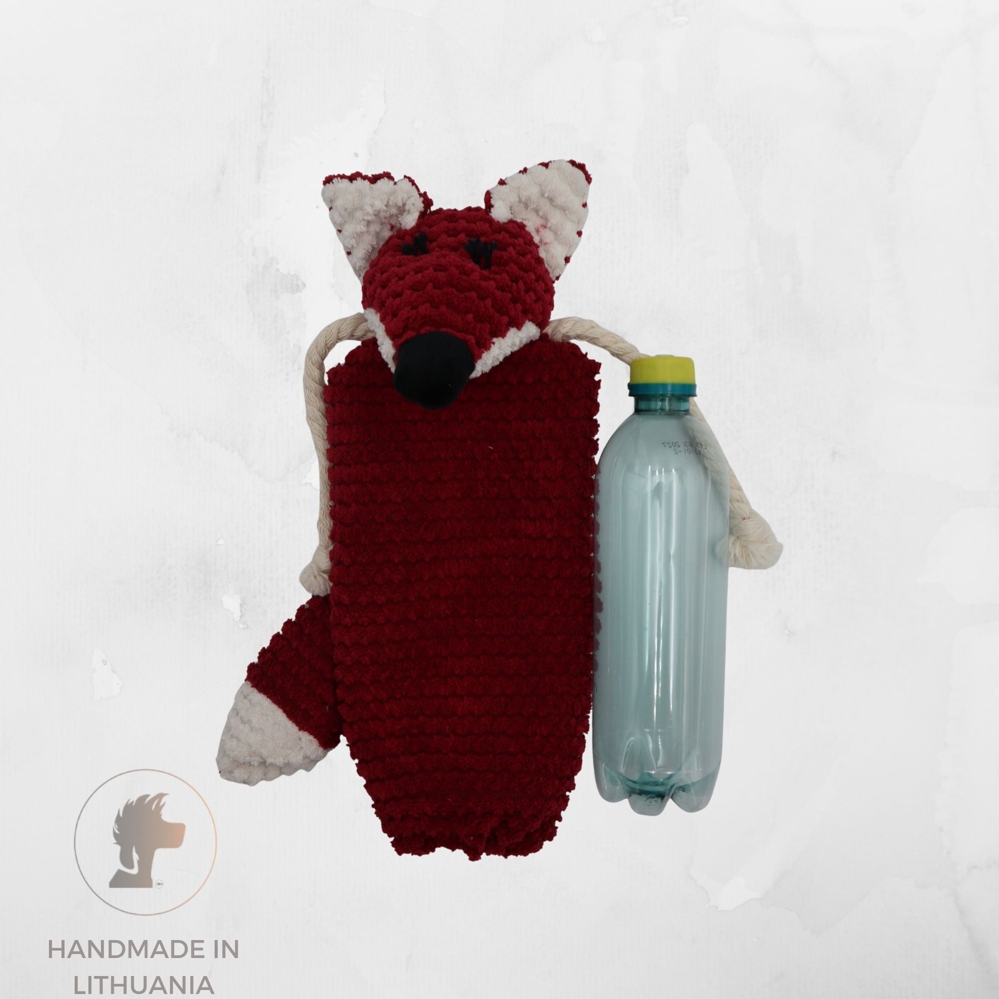 A handmade crocheted fox-shaped pouch or bag in deep red and cream, shown holding a clear plastic bottle to demonstrate scale. The background is a textured light gray surface with a 'Handmade in Lithuania' logo in the bottom-left corner.