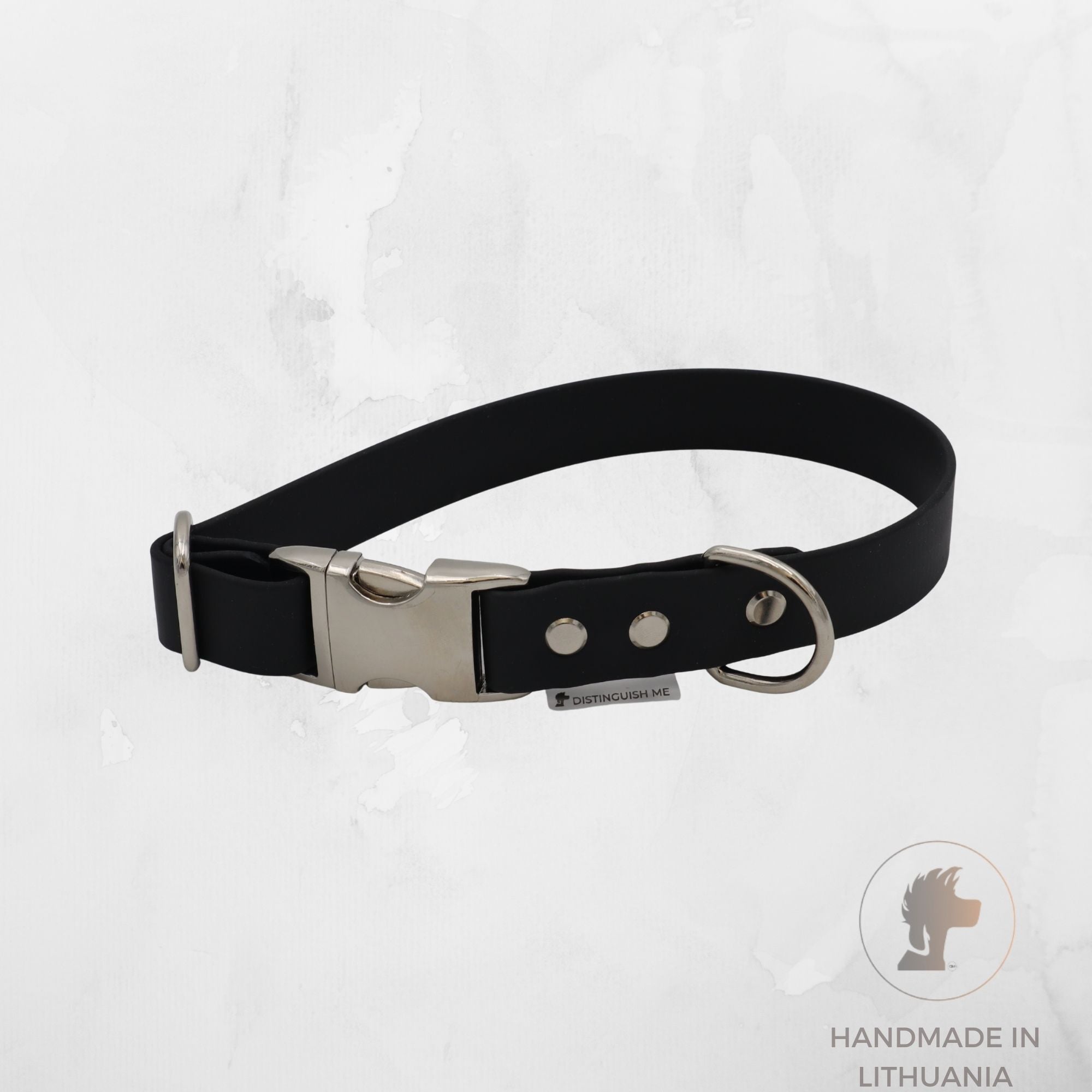 A black  dog collar with a silver-tone metal buckle, D-ring, and rivets, displayed on a light gray textured background with a 'Handmade in Lithuania' logo in the bottom right corner.