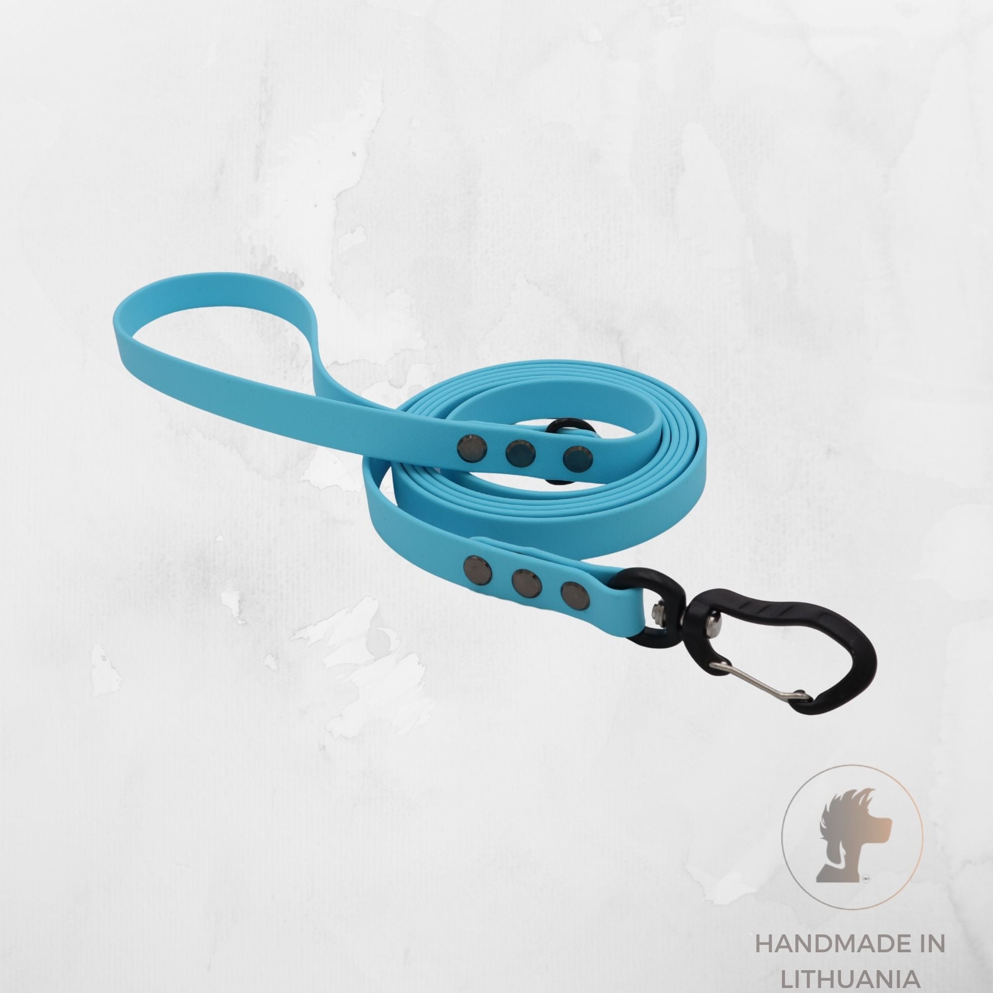 A bright blue pet leash with a black carabiner clip, coiled on a light gray textured background. A circular logo in the bottom right corner reads 'HANDMADE IN LITHUANIA' with a lion head icon.