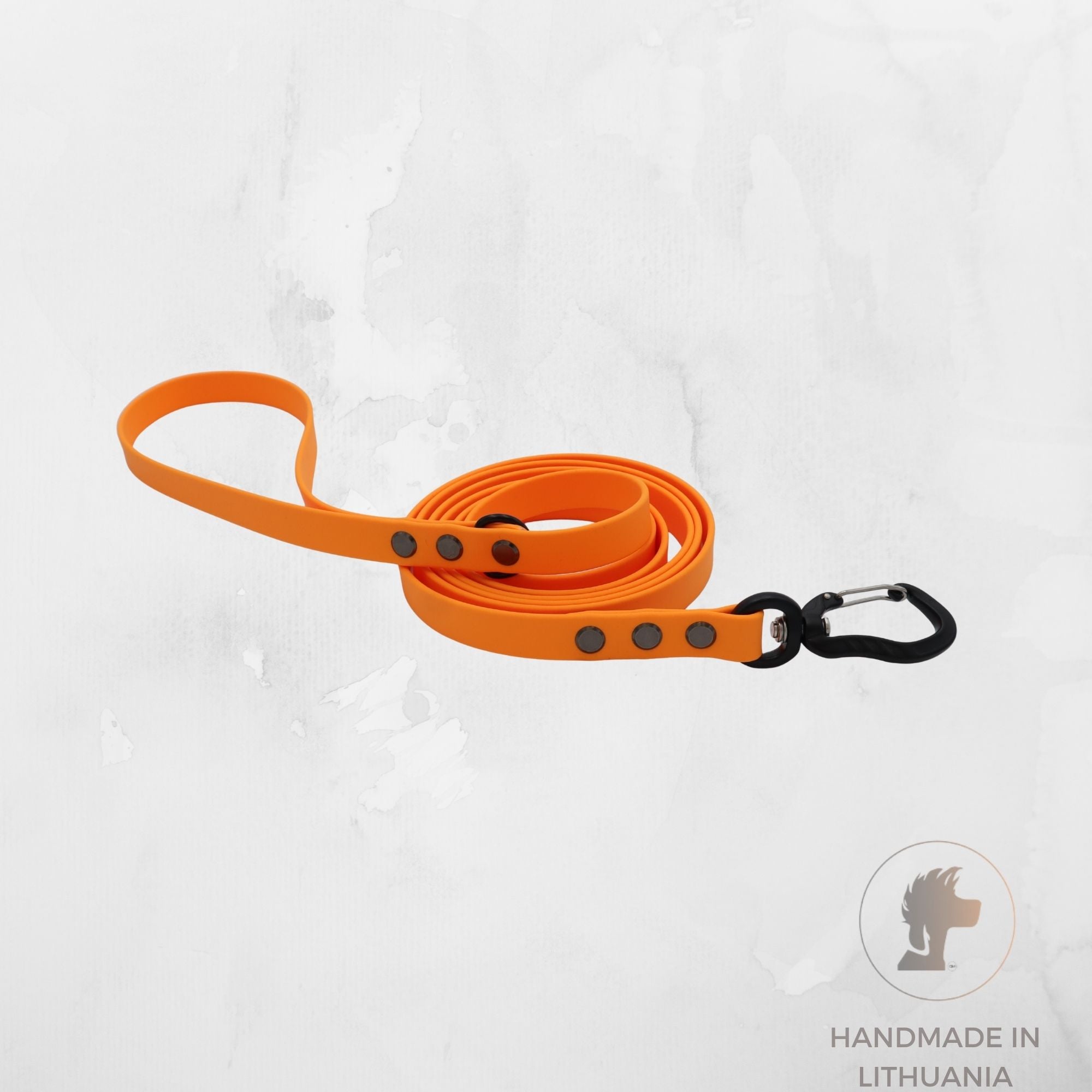 Bright orange dog leash with black metal hardware and a black carabiner clip, coiled on a light gray textured background with a 'Handmade in Lithuania' logo in the bottom right corner.