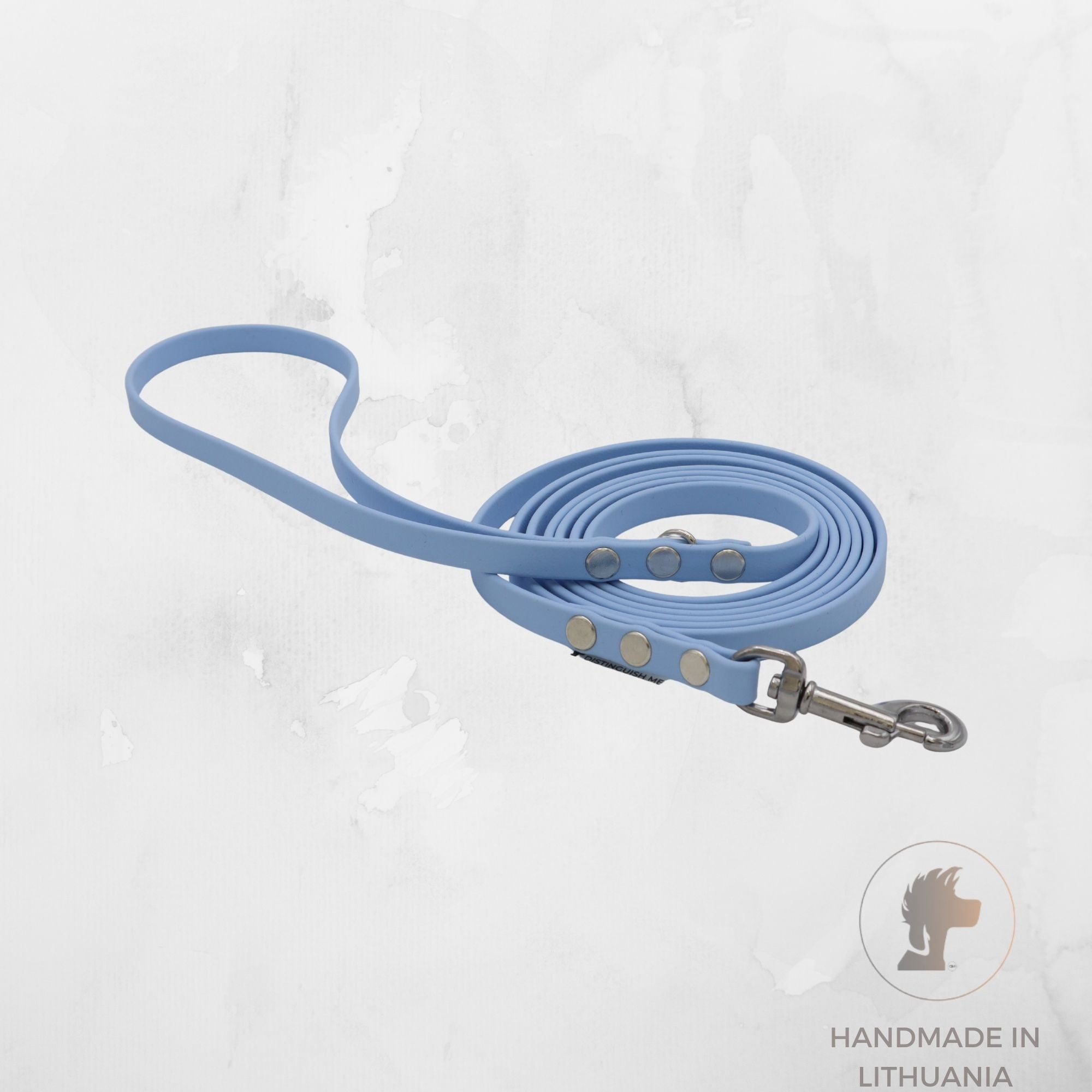 A light blue dog leash with silver metal hardware, coiled on a textured light gray background with a 'Handmade in Lithuania' logo in the bottom right corner.