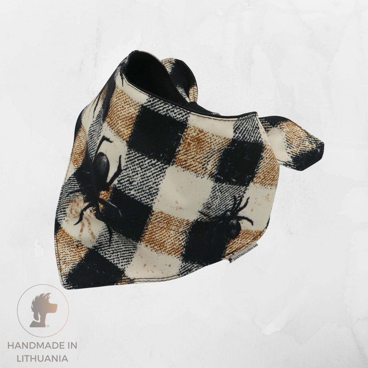 A handmade triangular pet bandana featuring a black, beige, and brown buffalo plaid pattern with black spider graphics, displayed on a light gray textured background.