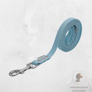 A light blue hexa dog leash with a silver metal swivel snap hook, neatly coiled on a textured light gray background. A circular logo in the bottom right corner reads 'HANDMADE IN LITHUANIA' with a dog silhouette.