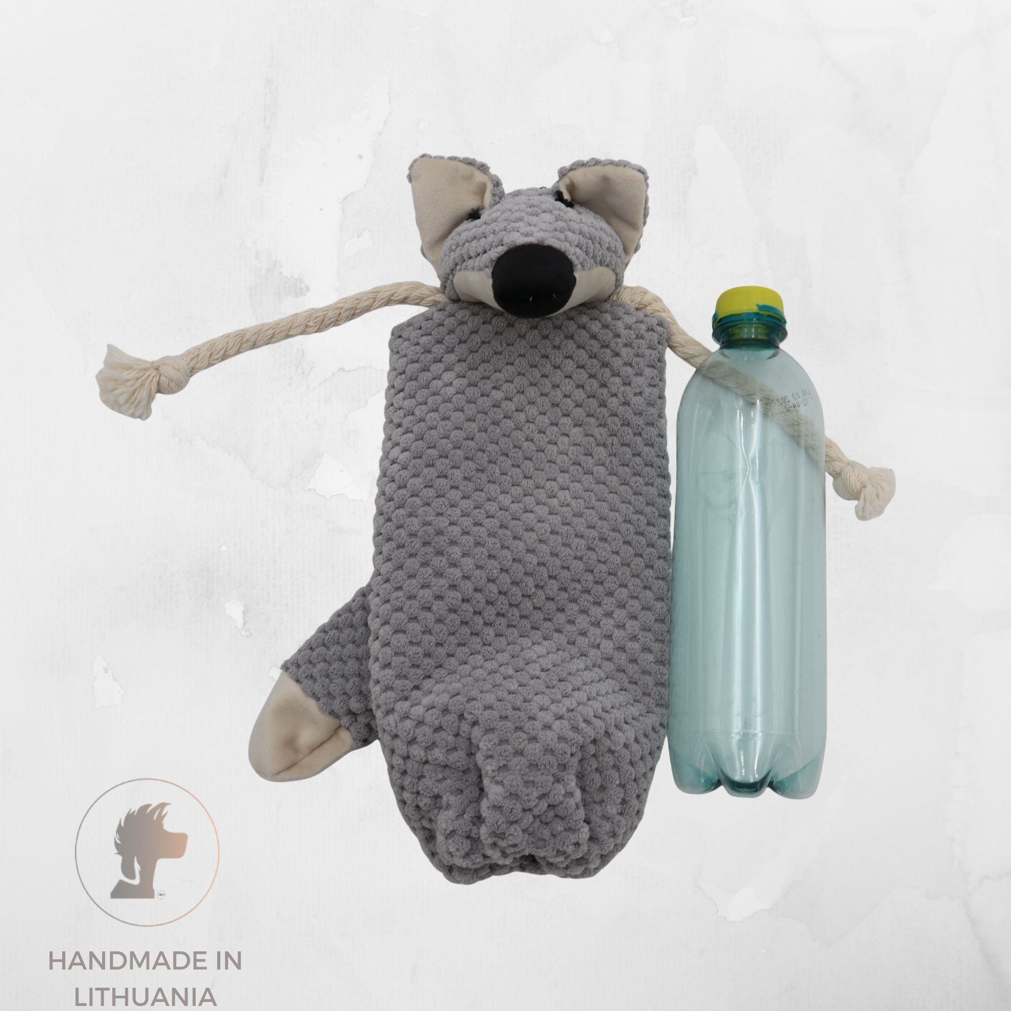 A handmade gray knitted wolf-shaped dog toy with rope tails and a plastic bottle attached to its side, shown against a light textured background with a 'Handmade in Lithuania' logo in the bottom-left corner.